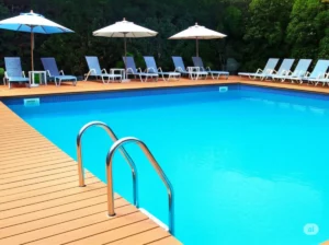 A vibrant, high-definition image of a sparkling inground swimming pool in a Buffalo backyard setting, with no faces visible, subtly incorporating KDpool elements. The photo showcases a clean and inviting pool design, with clear blue water and well-maintained surrounding landscaping, possibly including a patio area with lounge chairs and umbrellas. The overall impression is one of quality and leisure. The focus is on the pool itself and its immediate surroundings, suggesting the investment involved in creating such a backyard amenity in Buffalo. The lighting is natural and bright, emphasizing the clear water and the textures of the pool and decking materials.